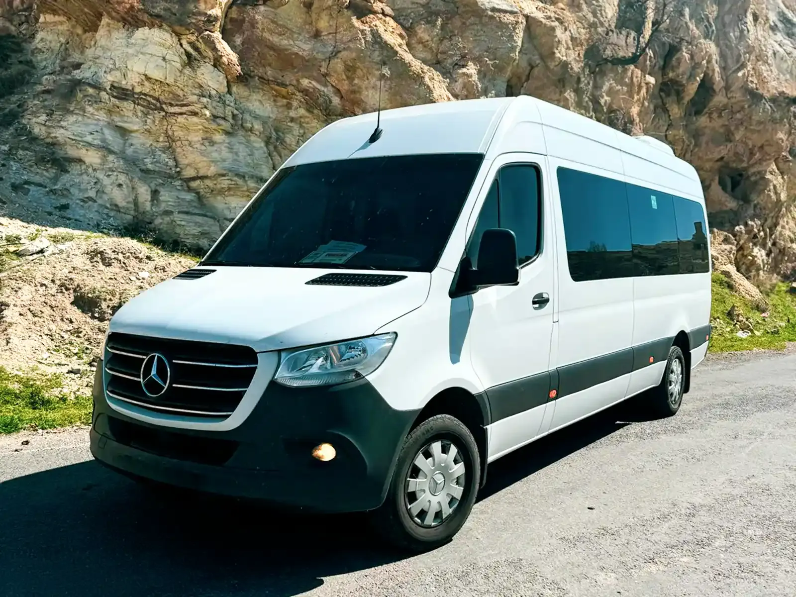Mercedes Sprinter shuttle bus parked against Cappadocia rock formations, three-quarter front view