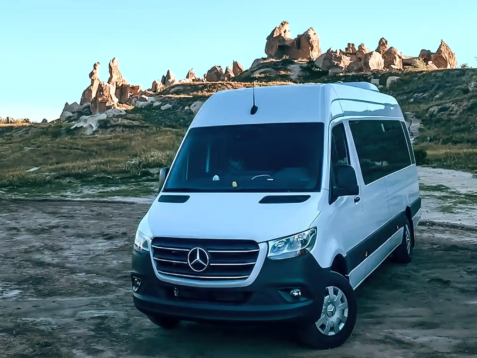 White Mercedes Sprinter private transfer van parked in Cappadocia landscape with fairy chimneys at sunset