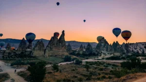 Colorful balloons rising over fairy chimneys at sunrise, showcasing which valleys do Cappadocia hot air balloons fly over.
