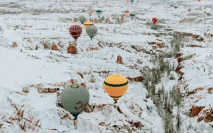 Balloons flying over snow-covered valleys, illustrating winter Cappadocia hot air balloon cancellation weather.