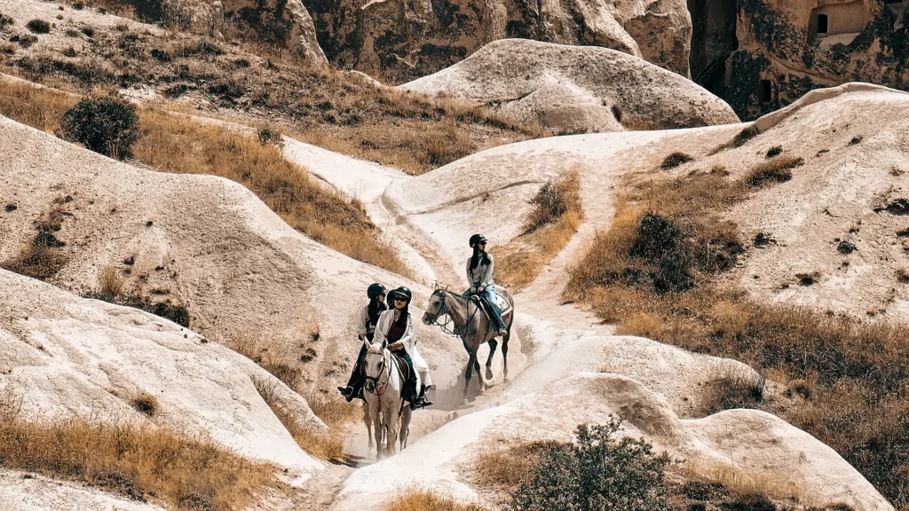 A guided group enjoying their first time horse riding in Cappadocia through the vast, rock-strewn Rose Valley at sunrise.