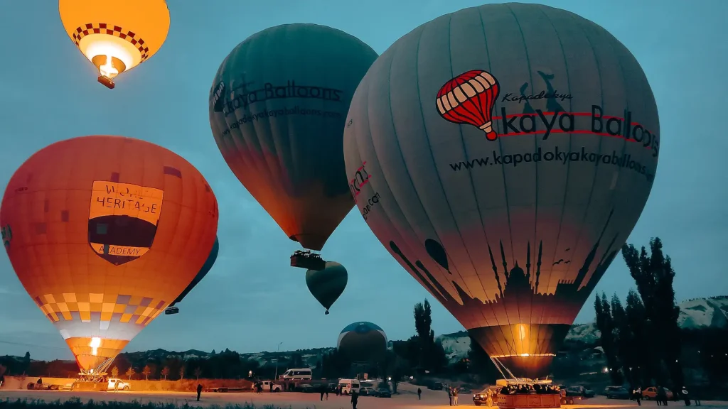 SHGM-licensed Cappadocia hot air balloons at sunrise launch — Kapadokya Kaya Balloons and World Heritage Academy preparing for flight over Göreme UNESCO site