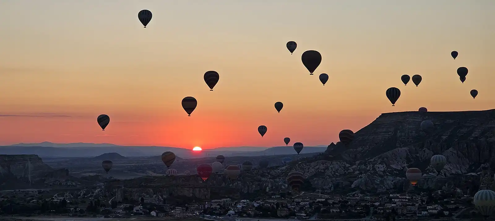 Hot air balloons rising over Göreme at sunrise, seen from the valley rim in Cappadocia