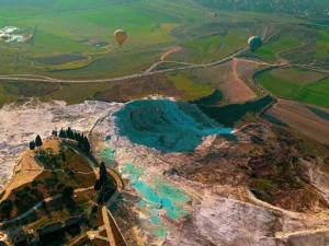 Aerial view of Pamukkale's turquoise thermal pools and travertine formations during a hot air balloon flight over Denizli valley farmland.