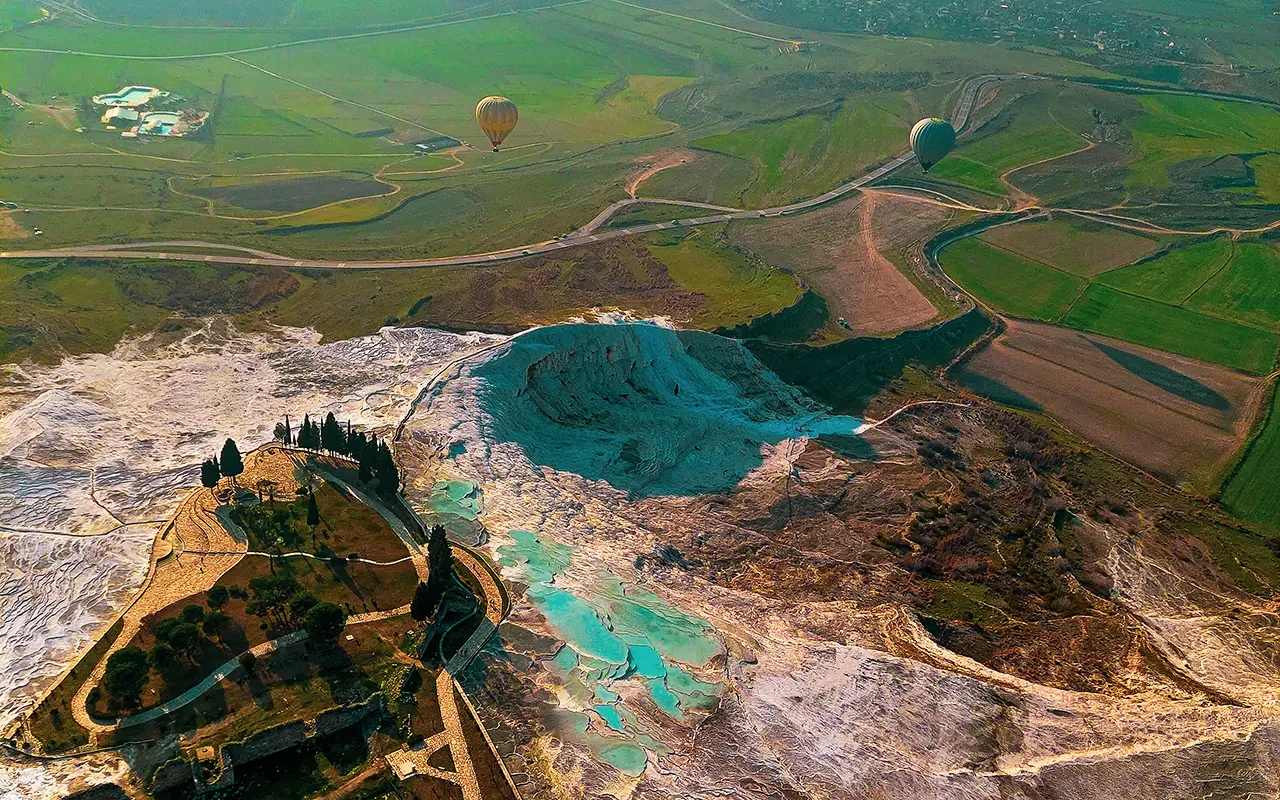 Aerial view of Pamukkale's turquoise thermal pools and travertine formations during a hot air balloon flight over Denizli valley farmland.